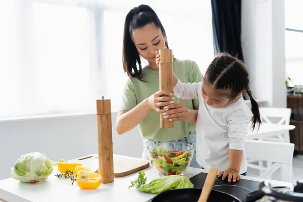 Asian mother and daughter seasoning salad in bowl — Stock Photo