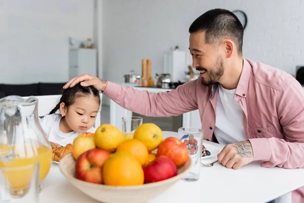 Heureux père caressant cheveux de asiatique fille pendant le petit déjeuner — Photo de stock