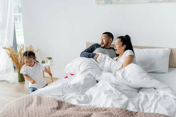Shocked asian parents looking at toddler daughter running in bedroom — Stock Photo