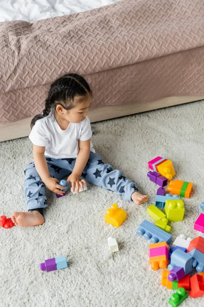 Alto ángulo vista de asiático niño jugando bloques de construcción en la alfombra en dormitorio - foto de stock