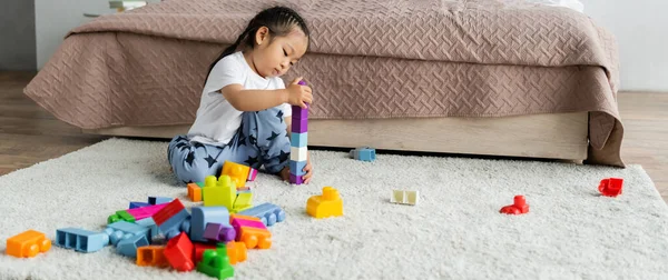 Asiatique tout-petit fille jouer blocs de construction sur tapis dans chambre, bannière — Photo de stock