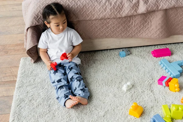 Alto ángulo vista de asiático niño niña jugando bloques de construcción en la alfombra en dormitorio - foto de stock