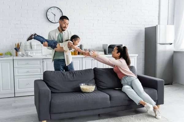 Asiatischer Vater hält Tochter in der Nähe seiner Frau auf Couch — Stockfoto