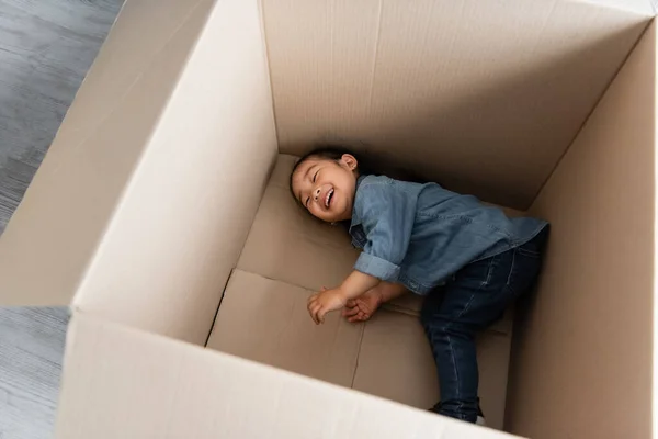 High angle view of happy asian toddler girl lying in empty carton box — Stock Photo