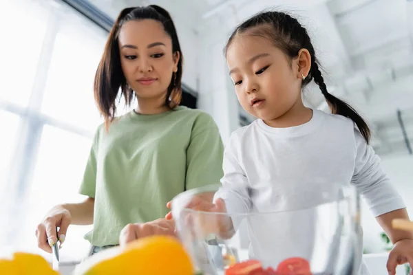 Bajo ángulo vista de asiático niño niña preparando ensalada con madre - foto de stock