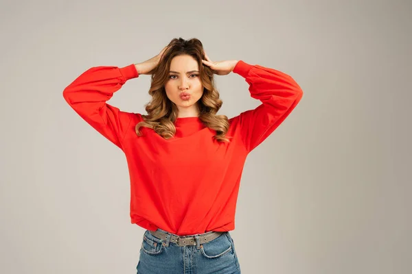 Curly woman with duck face adjusting hair isolated on grey — Stock Photo