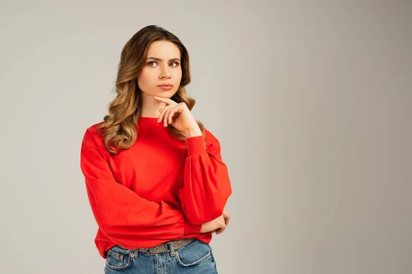 Pensive woman in red sweatshirt looking away and thinking isolated on grey — Stock Photo