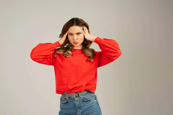 Pensive woman with duck face adjusting hair isolated on grey — Stock Photo