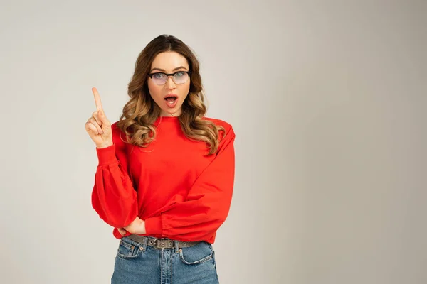 Shocked woman in sweatshirt and eyeglasses pointing with finger isolated on grey — Stock Photo
