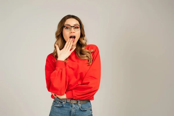 Femme choquée en sweat-shirt et lunettes à bouche ouverte isolé sur gris — Photo de stock