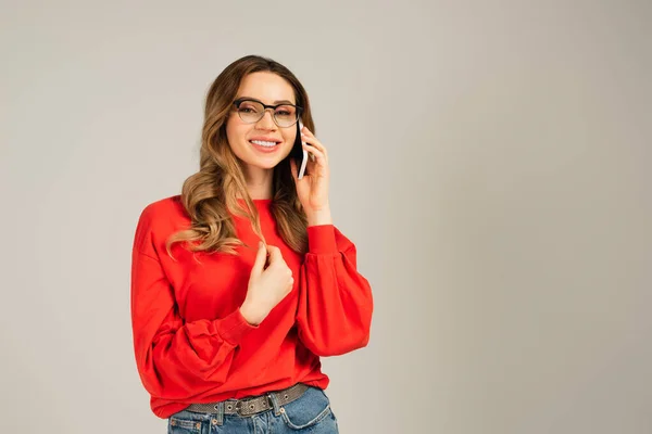 Mujer alegre en gafas que habla en el teléfono celular aislado en gris - foto de stock