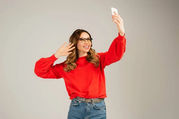 Glückliche Frau in Brille und Sweatshirt mit Videoanruf auf Smartphone isoliert auf grau — Stockfoto