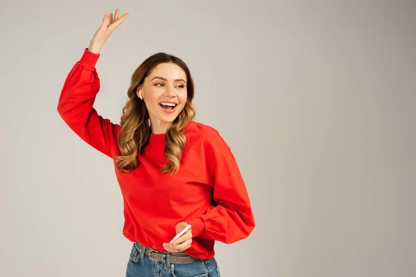 Excited woman in wireless earphones holding smartphone isolated on grey — Stock Photo