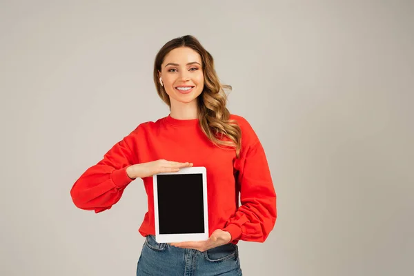 Mujer alegre en auriculares inalámbricos sosteniendo tableta digital con pantalla en blanco aislado en gris — Stock Photo