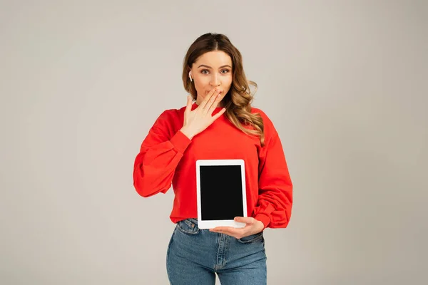 Überraschte Frau in drahtlosen Kopfhörern hält digitales Tablet mit leerem Bildschirm isoliert auf grau — Stockfoto