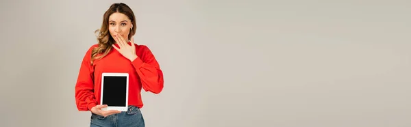 Mujer sorprendida en auriculares inalámbricos sosteniendo tableta digital con pantalla en blanco aislada en gris, bandera - foto de stock