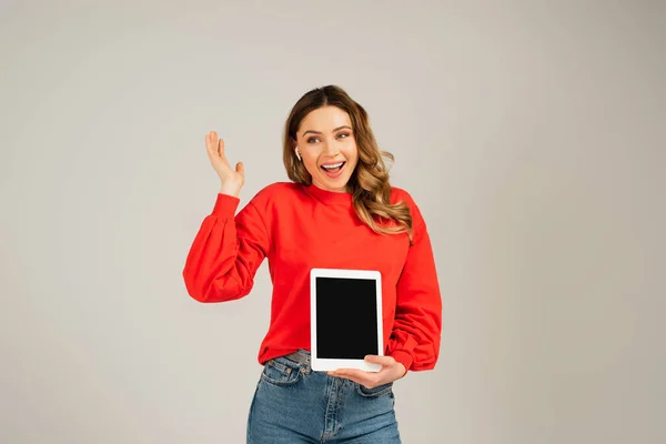 Mujer sorprendida en auriculares inalámbricos sosteniendo tableta digital con pantalla en blanco aislada en gris - foto de stock