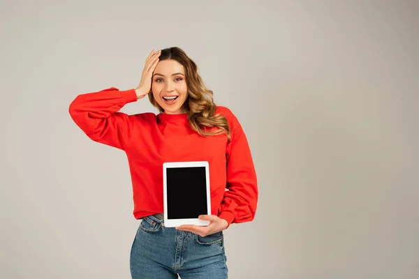 Mujer sorprendida sosteniendo tableta digital con pantalla en blanco aislada en gris - foto de stock