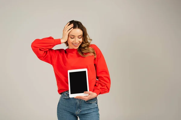 Mujer alegre mirando la tableta digital con la pantalla en blanco aislada en gris - foto de stock