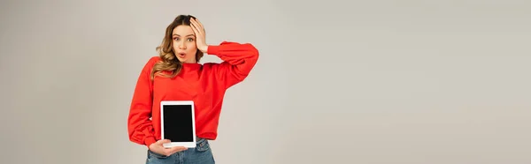 Шокована жінка тримає цифровий планшет з порожнім екраном ізольовано на сірому, банер — стокове фото