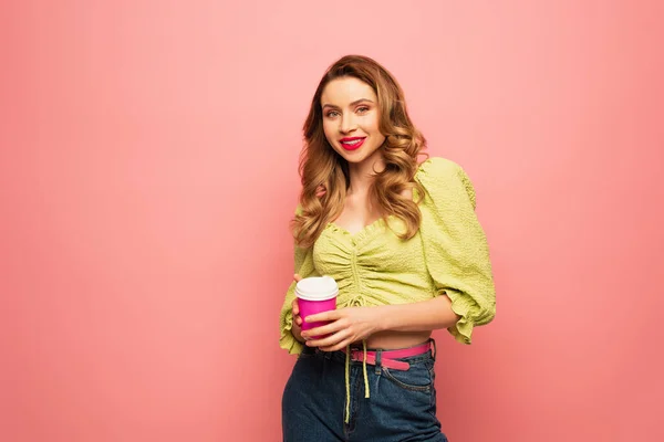 Glückliche Frau in grüner Bluse mit Kaffee to go auf rosa — Stockfoto