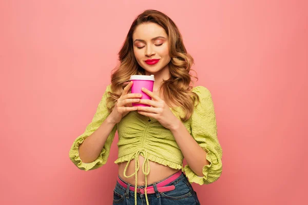 Femme heureuse en chemisier vert sentant le café pour aller isolé sur rose — Photo de stock