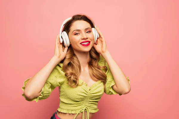 Mujer feliz ajustando auriculares inalámbricos aislados en rosa - foto de stock