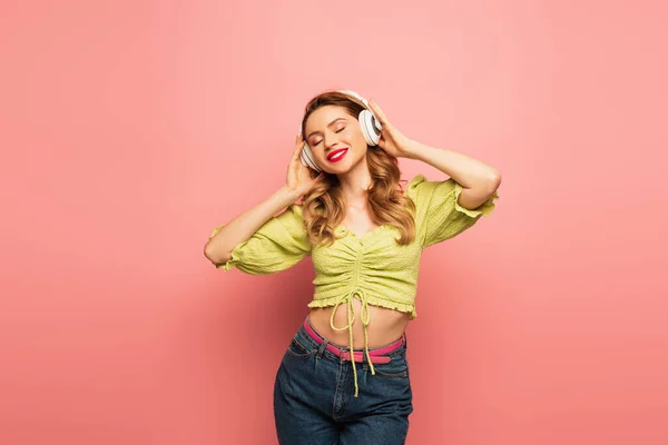 Lächelnde Frau stellt drahtlose Kopfhörer auf rosa — Stockfoto