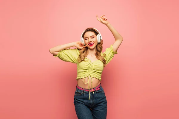 Fröhliche Frau mit drahtlosen Kopfhörern, die auf rosa tanzt — Stockfoto