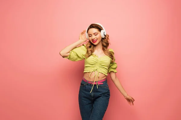 Позитивна жінка регулює бездротові навушники на рожевому — стокове фото