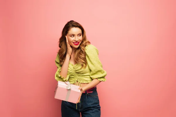 Счастливая женщина держит завернутый подарок изолирован на розовый — стоковое фото