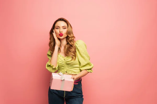 Curly woman with duck face holding wrapped present isolated on pink — Stock Photo