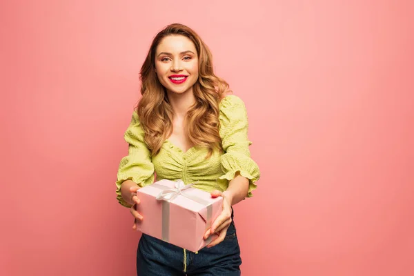Усміхнена жінка тримає загорнутий подарунок ізольовано на рожевому — стокове фото