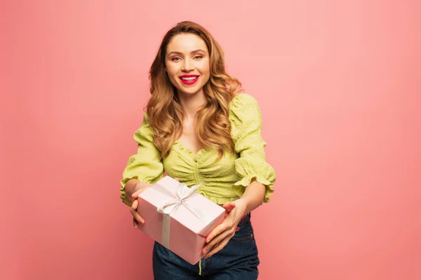 Positive woman holding wrapped present isolated on pink — Stock Photo