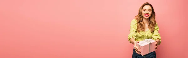 Mulher positiva segurando presente envolto isolado em rosa, banner — Fotografia de Stock