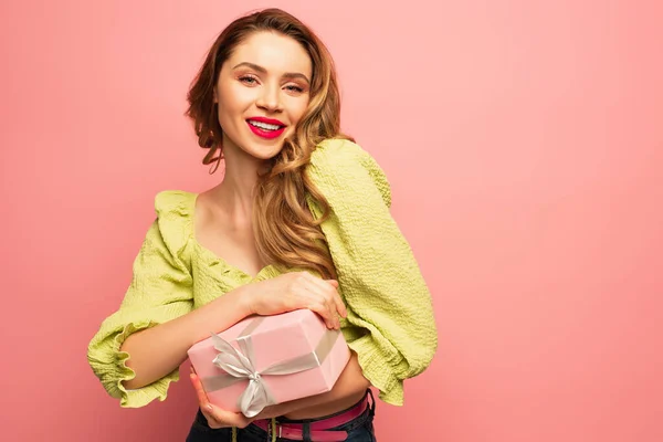 Mujer complacida sosteniendo envuelto caja de regalo aislado en rosa - foto de stock