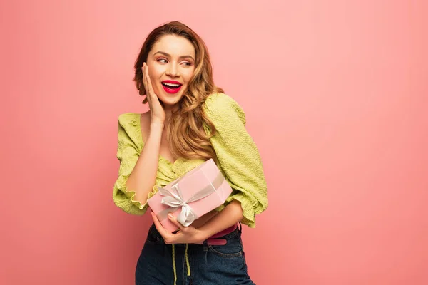 Excited woman holding wrapped gift box isolated on pink — Stock Photo