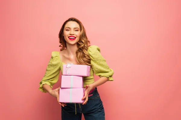 Щаслива жінка тримає загорнуті подарунки ізольовані на рожевому — стокове фото