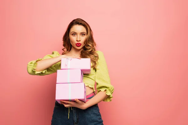 Lockige Frau mit Entengesicht hält umwickelte Geschenke isoliert auf rosa — Stockfoto