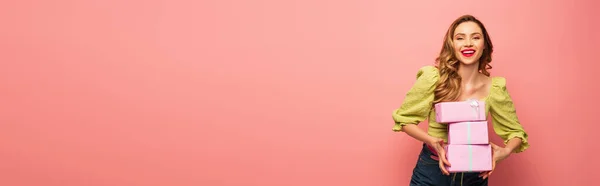 Mulher feliz segurando presentes embrulhados isolados em rosa, banner — Fotografia de Stock