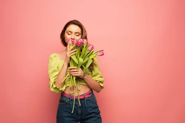 Erfreut Frau riecht Tulpen isoliert auf rosa — Stockfoto