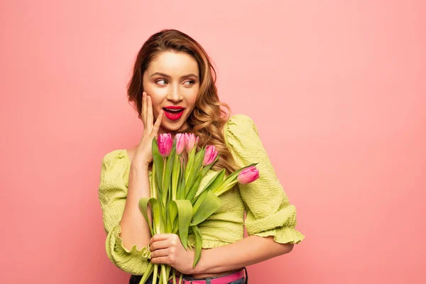 Mujer asombrada sosteniendo ramo de tulipanes aislados en rosa - foto de stock
