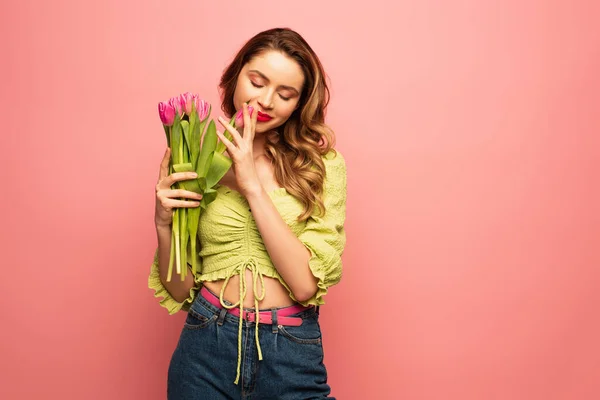 Mujer alegre oliendo tulipanes aislados en rosa - foto de stock