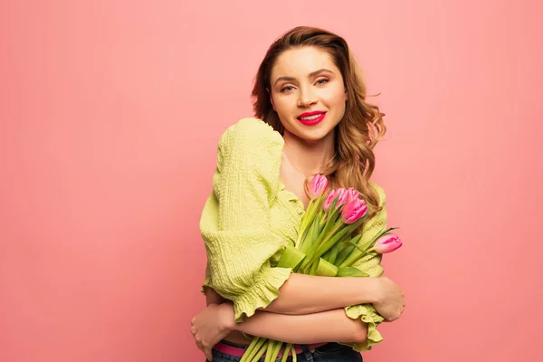 Femme bouclée souriante tenant bouquet de fleurs isolées sur rose — Photo de stock