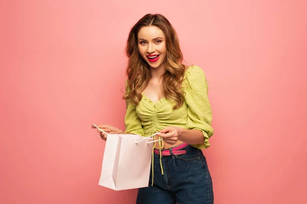 Glückliche Frau in grüner Bluse mit Einkaufstasche auf rosa — Stockfoto