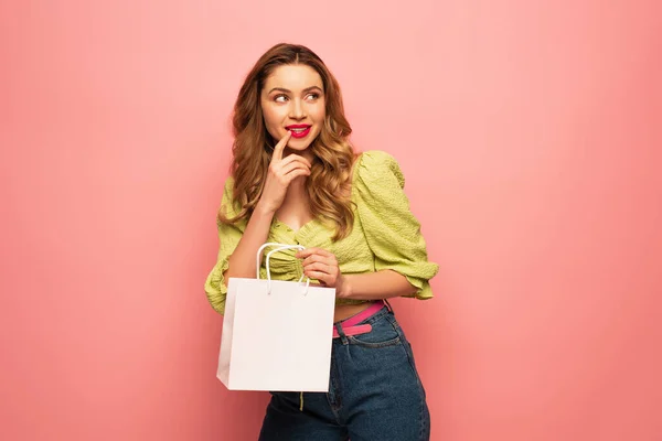 Curious woman in green blouse holding shopping bag and looking away isolated on pink — Stock Photo