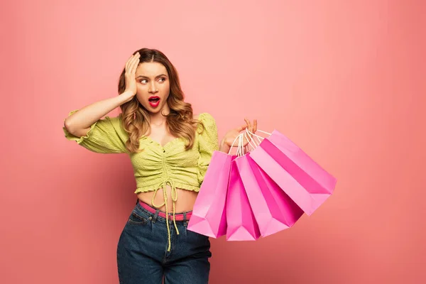 Donna scioccata che tiene borse della spesa isolate su rosa — Foto stock