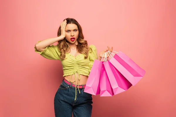 Donna scioccata tenendo borse della spesa e guardando la fotocamera isolata su rosa — Foto stock