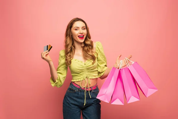 Mujer sorprendida sosteniendo tarjetas de crédito y bolsas de compras aisladas en rosa - foto de stock