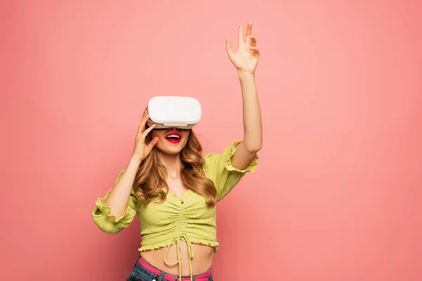Excited woman in vr headset with raised hand gesturing isolated on pink — Stock Photo